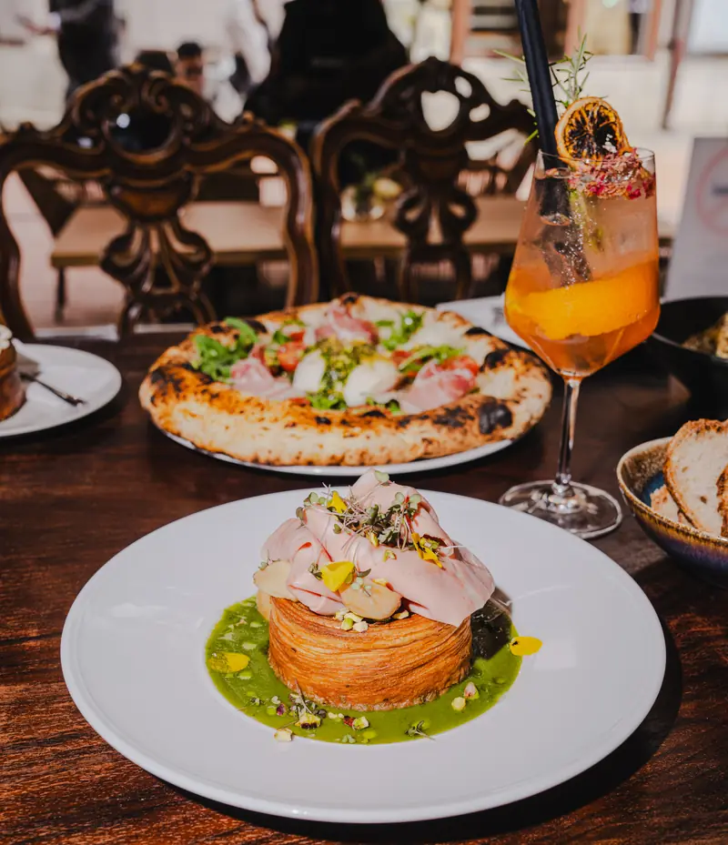 Töltött croissant zöld mártáson, mögötte nápolyi pizza és spritz